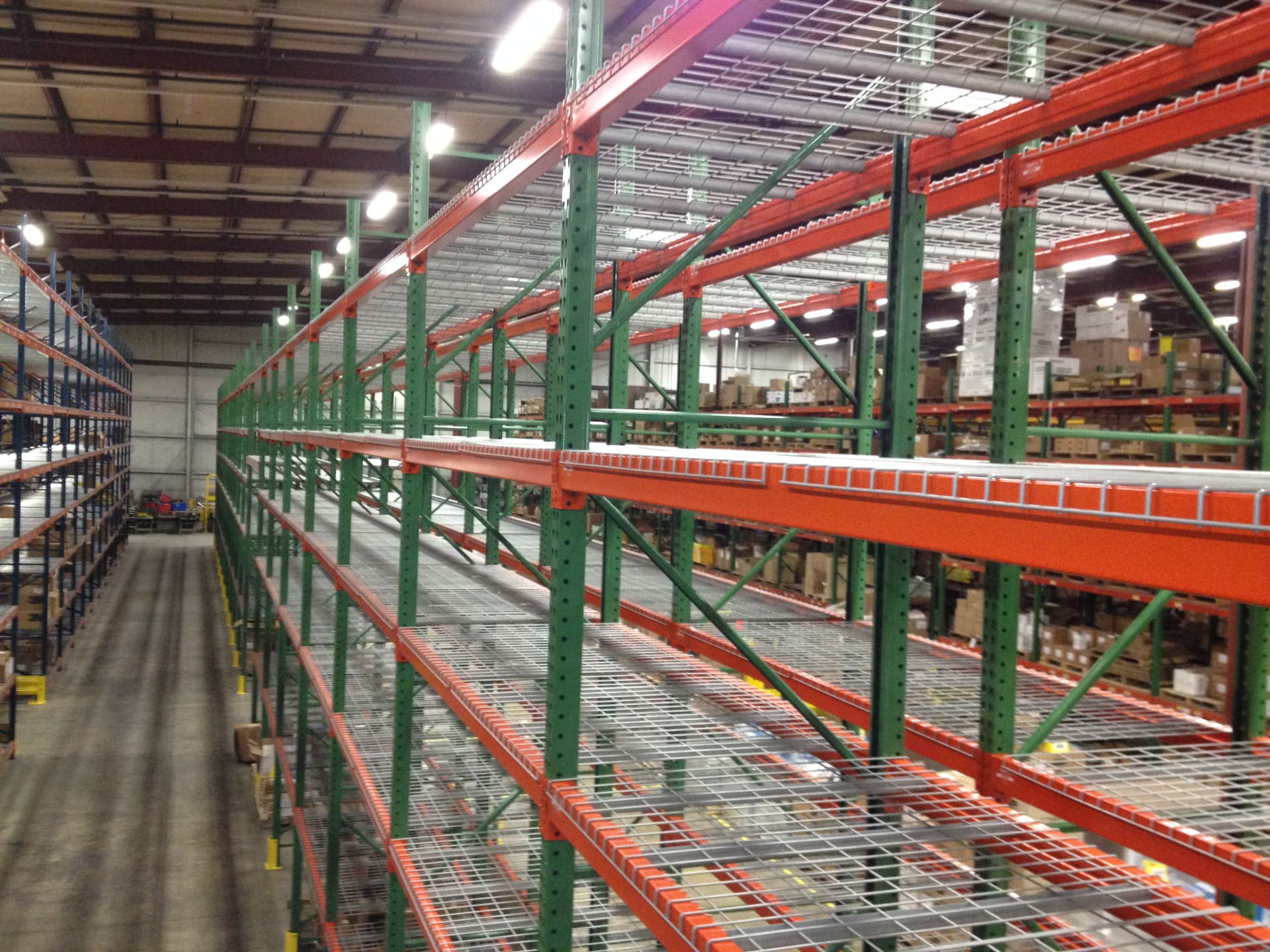 Rows of selective pallet racking with green uprights and orange beams down a warehouse aisle