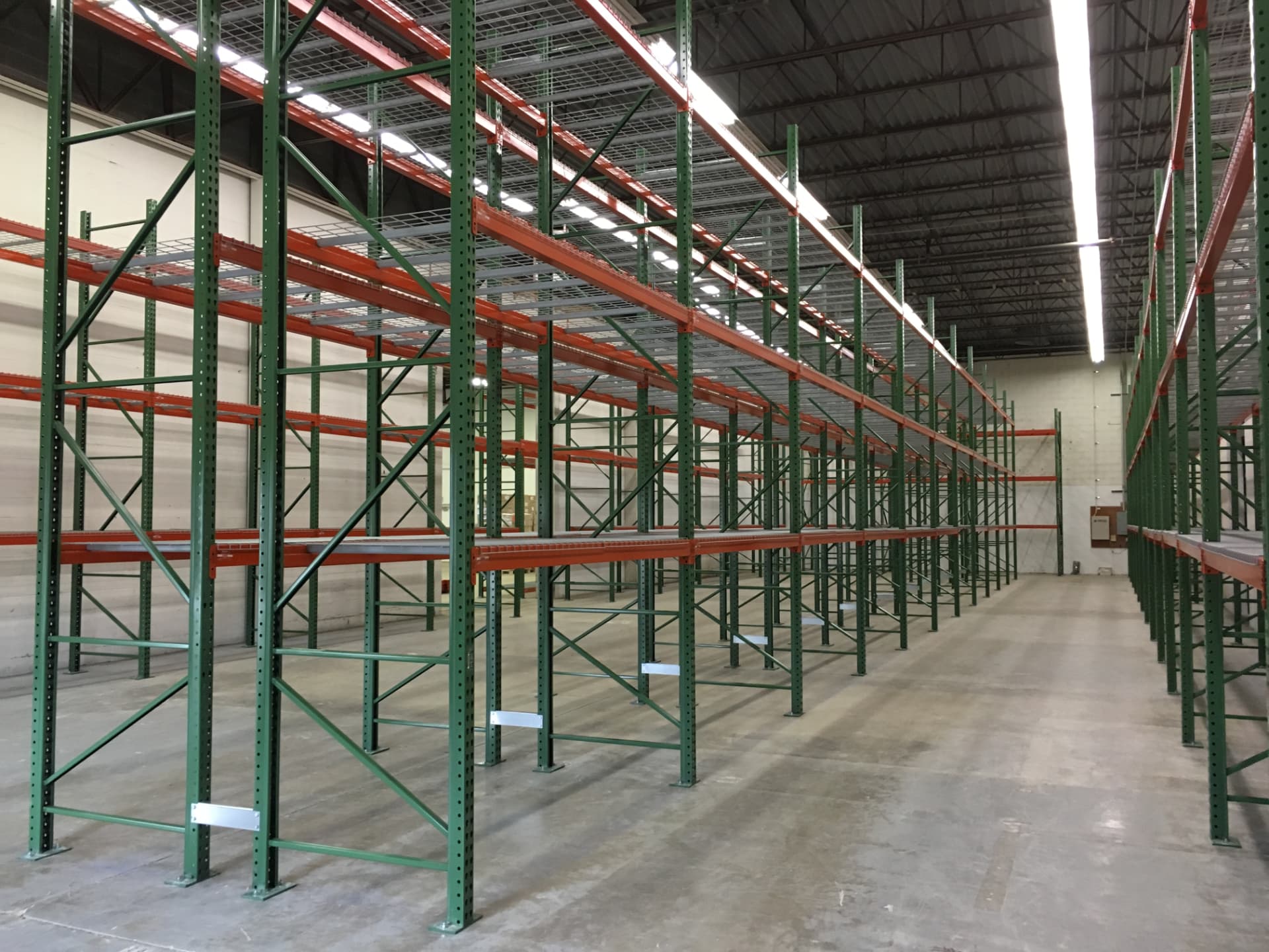 Long rows of green and orange pallet racking installed on a concrete warehouse floor