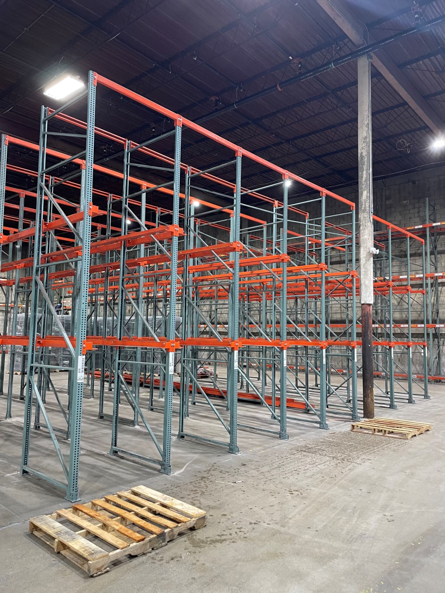 Drive-in pallet rack system with tall uprights and orange rails in an open warehouse