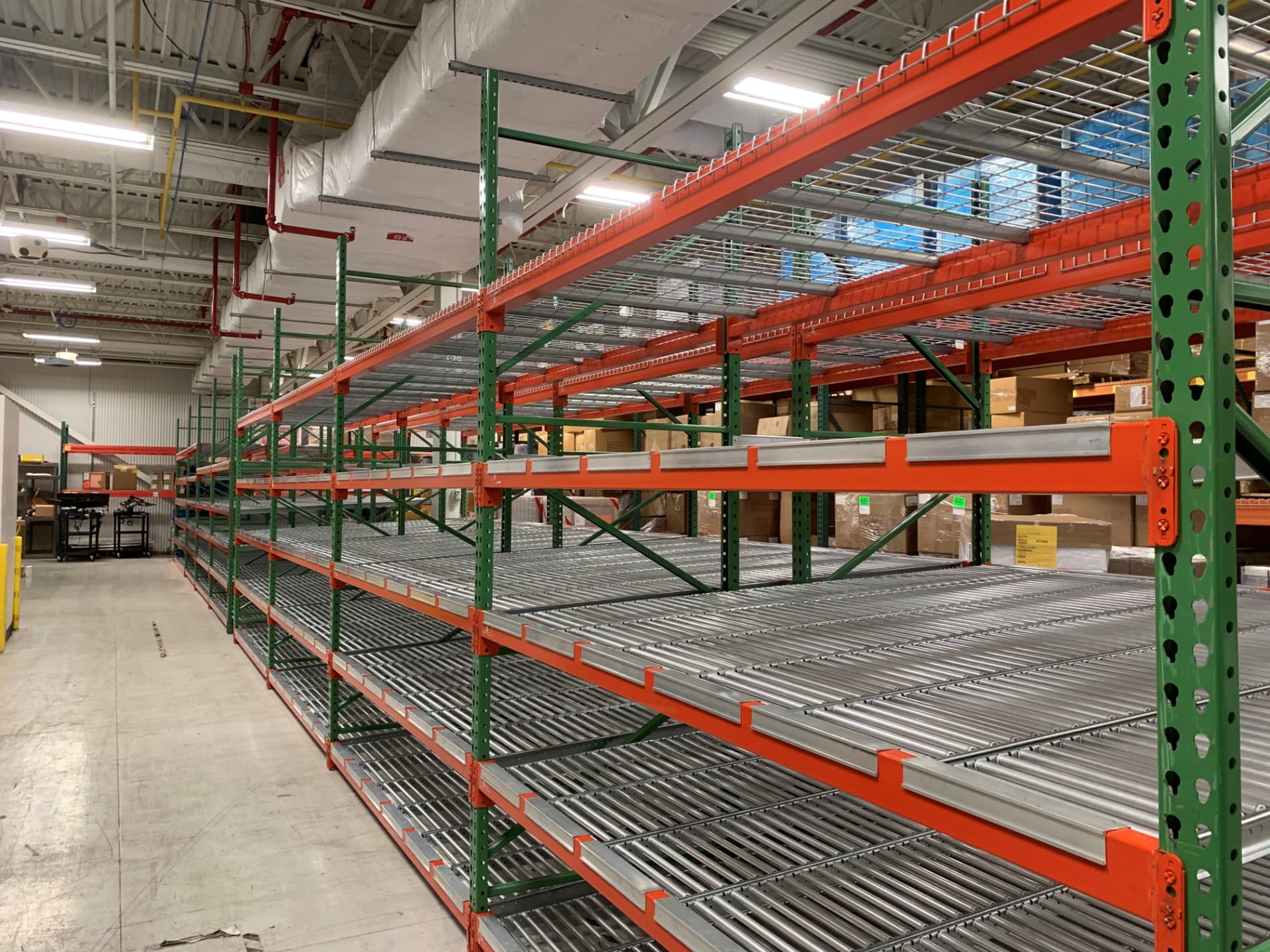 Carton flow racking with roller tracks and orange beams installed in a distribution warehouse